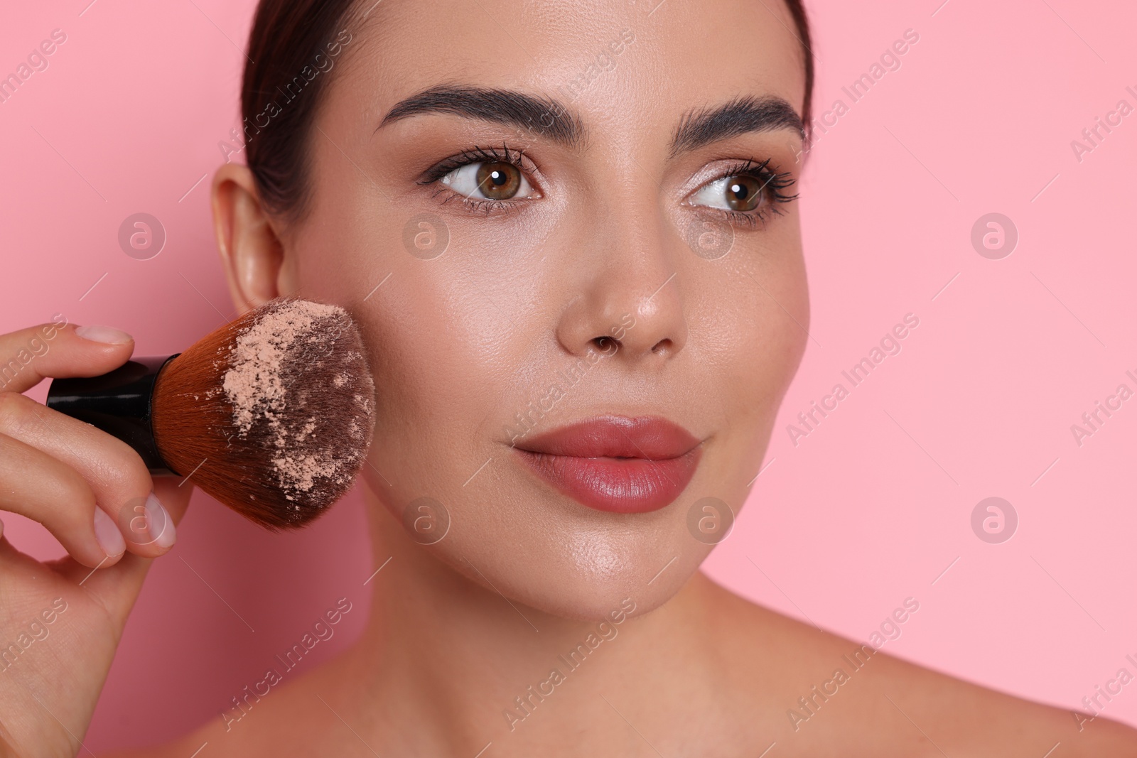 Photo of Beautiful woman applying makeup with brush on pink background, closeup