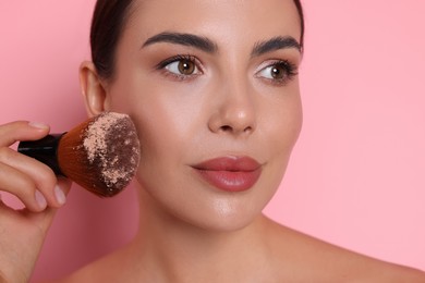 Photo of Beautiful woman applying makeup with brush on pink background, closeup