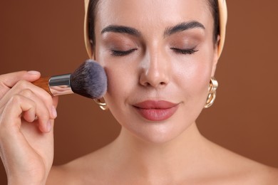 Photo of Beautiful woman applying makeup with brush on brown background, closeup