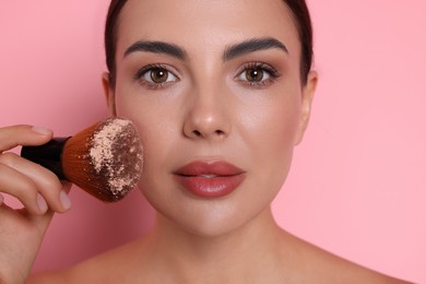 Photo of Beautiful woman applying makeup with brush on pink background, closeup