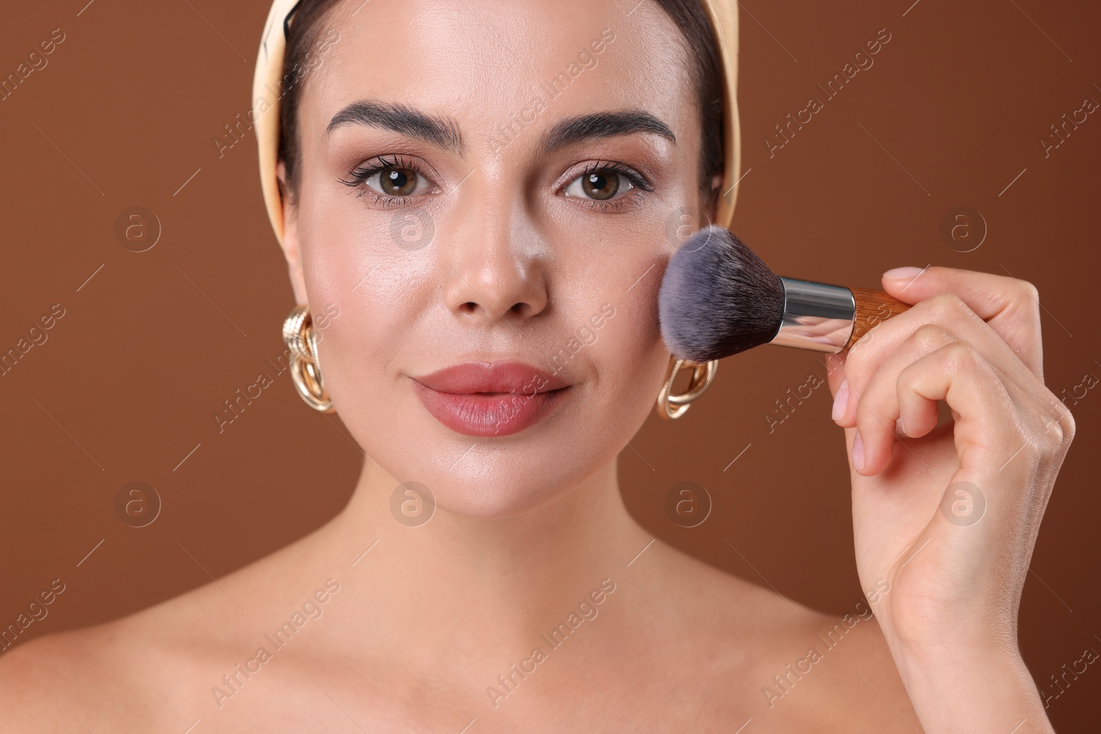 Photo of Beautiful woman applying makeup with brush on brown background