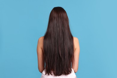 Photo of Woman with damaged hair before lamination procedure on light blue background, back view