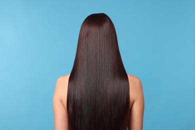 Photo of Woman with beautiful smooth hair after lamination procedure on light blue background, back view