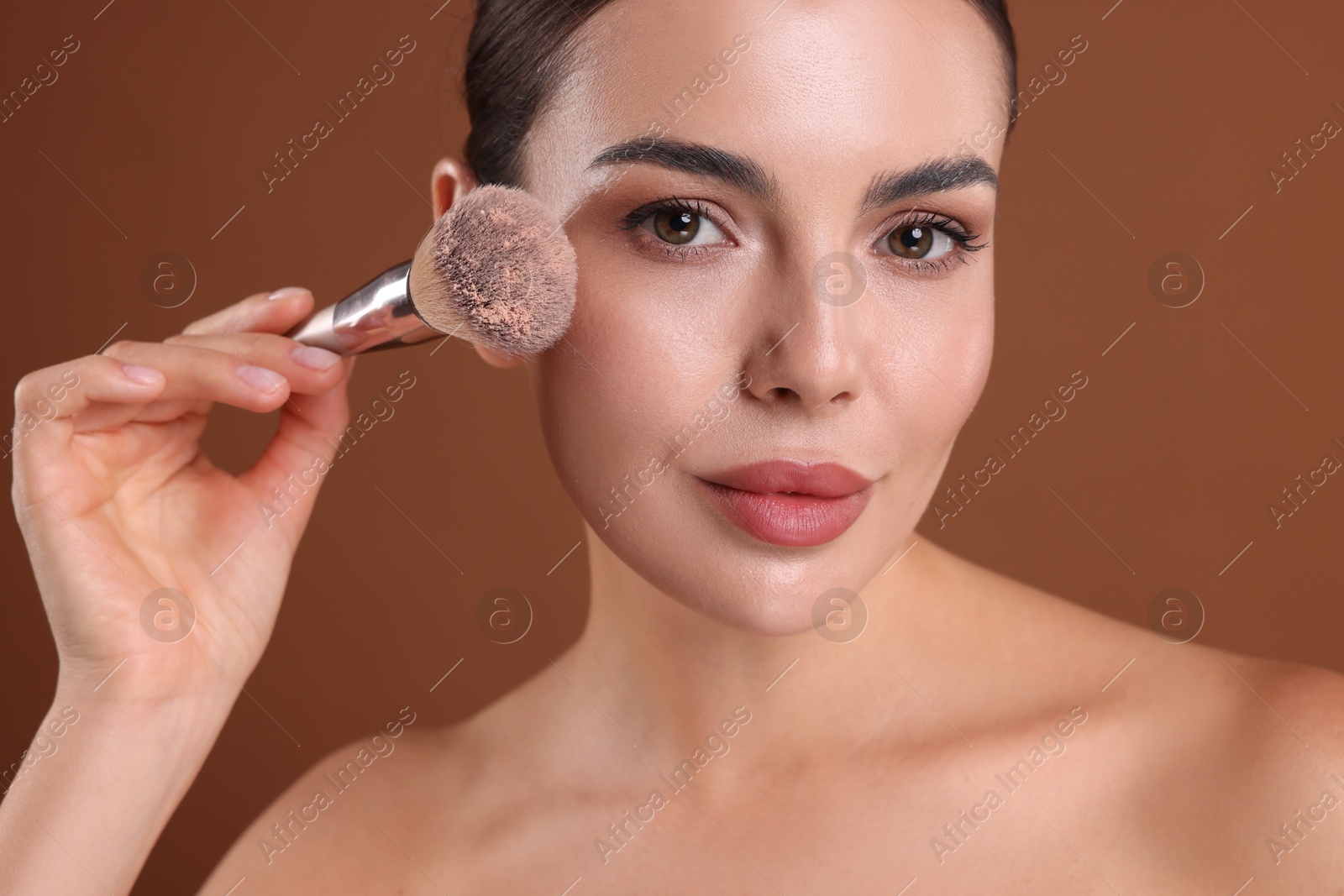 Photo of Beautiful woman applying makeup with brush on brown background