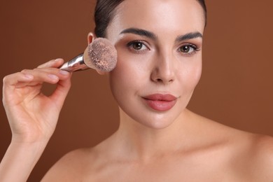 Photo of Beautiful woman applying makeup with brush on brown background