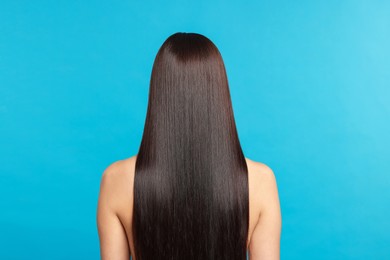 Photo of Woman with beautiful smooth hair after lamination procedure on light blue background, back view