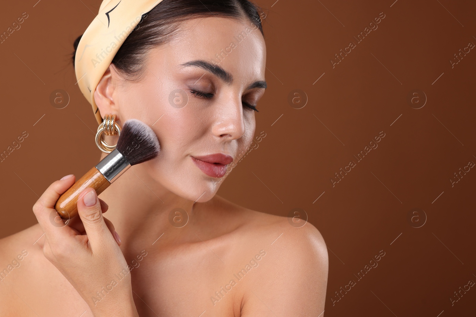 Photo of Beautiful woman applying makeup with brush on brown background, space for text