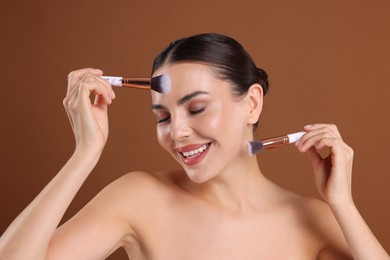 Photo of Beautiful woman with makeup brushes on brown background