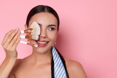 Photo of Beautiful woman with makeup brushes on pink background, space for text