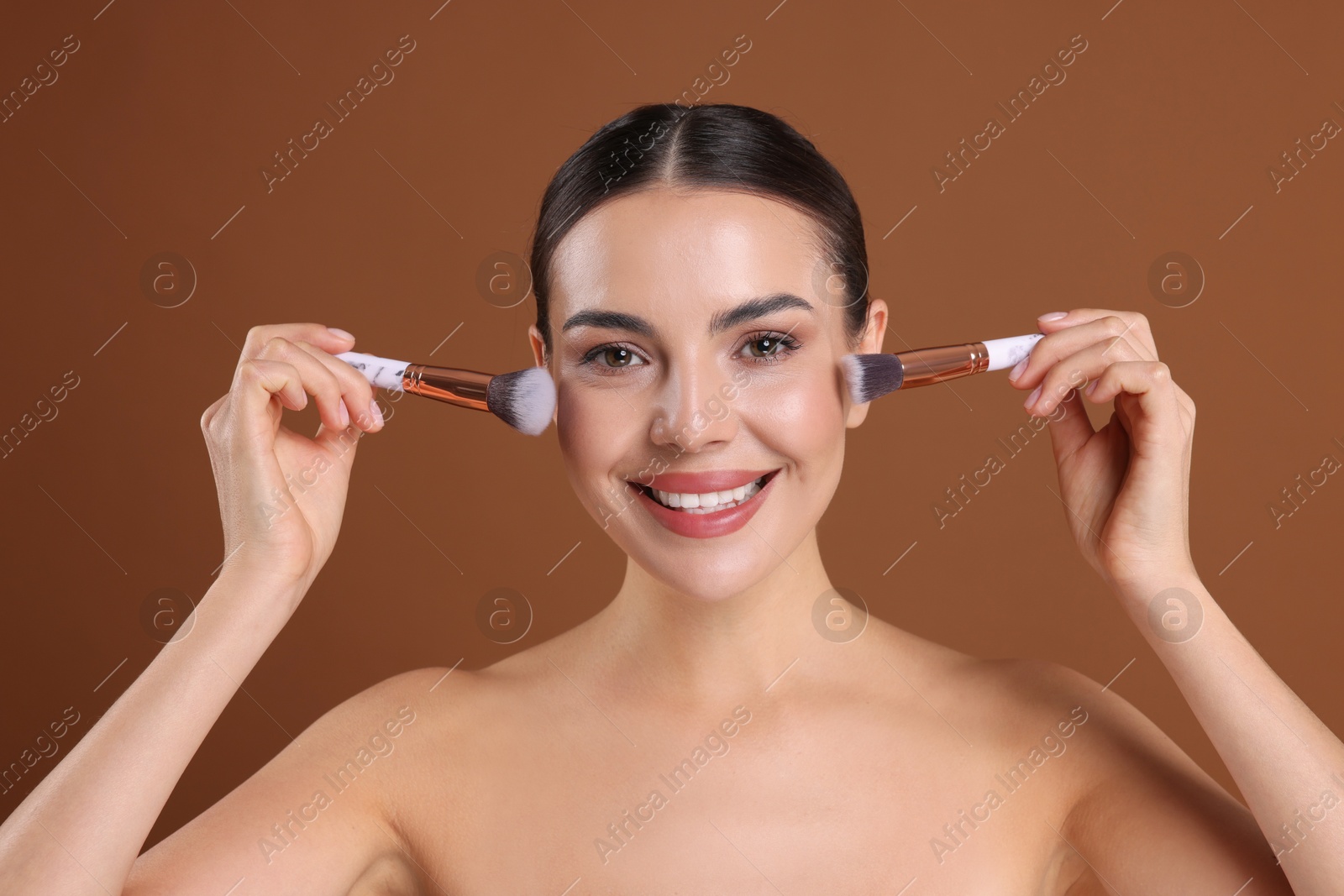 Photo of Beautiful woman with makeup brushes on brown background
