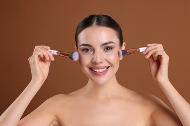 Photo of Beautiful woman with makeup brushes on brown background