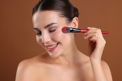 Photo of Beautiful woman applying makeup with brush on brown background