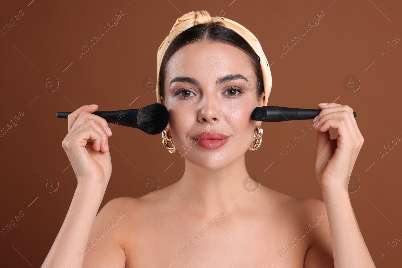 Photo of Beautiful woman with makeup brushes on brown background