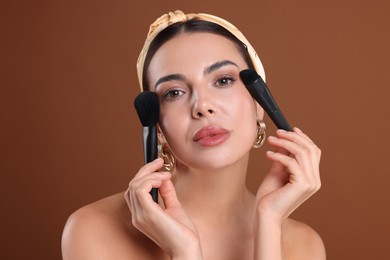 Photo of Beautiful woman with makeup brushes on brown background