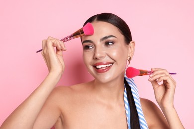Photo of Beautiful woman with makeup brushes on pink background