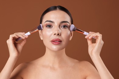 Photo of Beautiful woman with makeup brushes on brown background