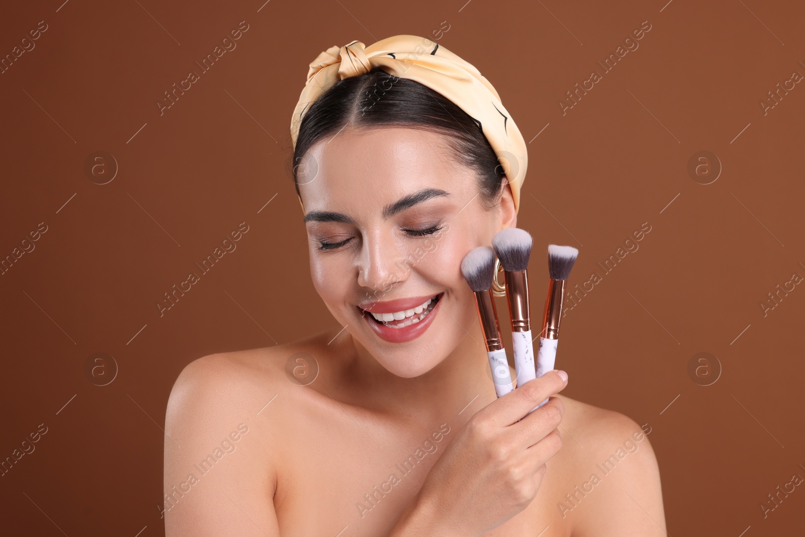 Photo of Beautiful woman with makeup brushes on brown background