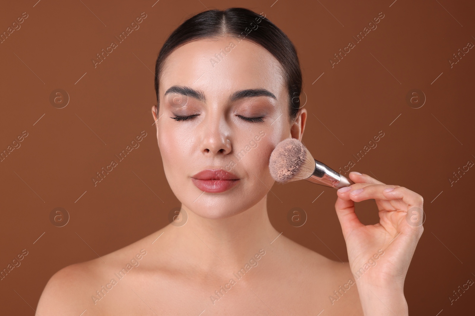 Photo of Beautiful woman applying makeup with brush on brown background
