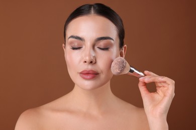 Photo of Beautiful woman applying makeup with brush on brown background