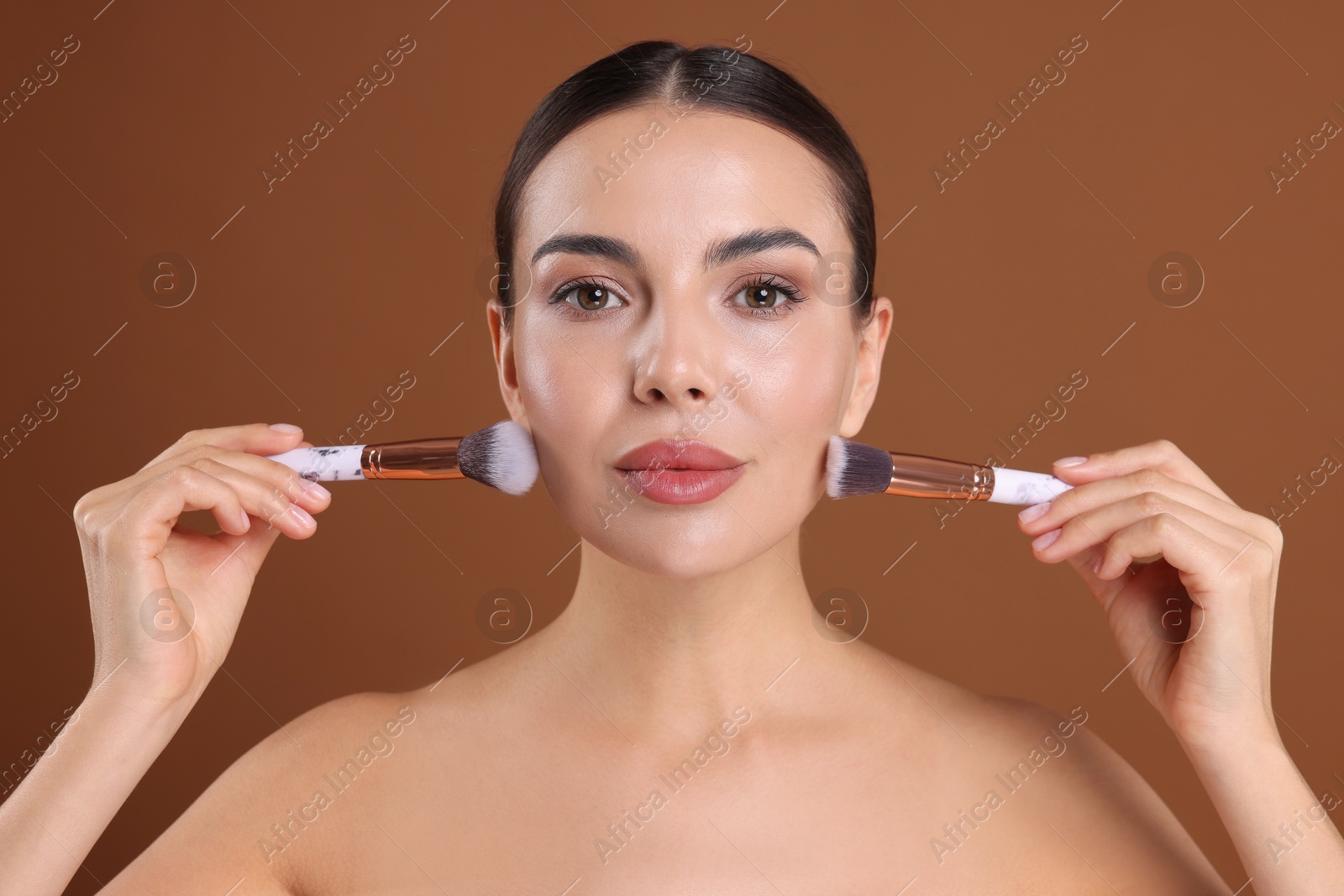 Photo of Beautiful woman with makeup brushes on brown background