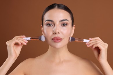 Photo of Beautiful woman with makeup brushes on brown background