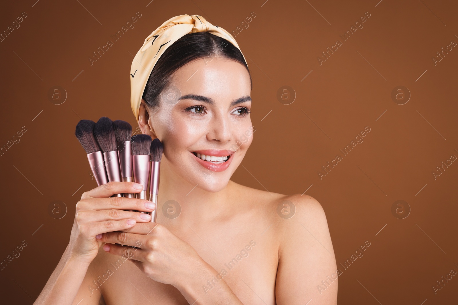 Photo of Beautiful woman with makeup brushes on brown background, space for text