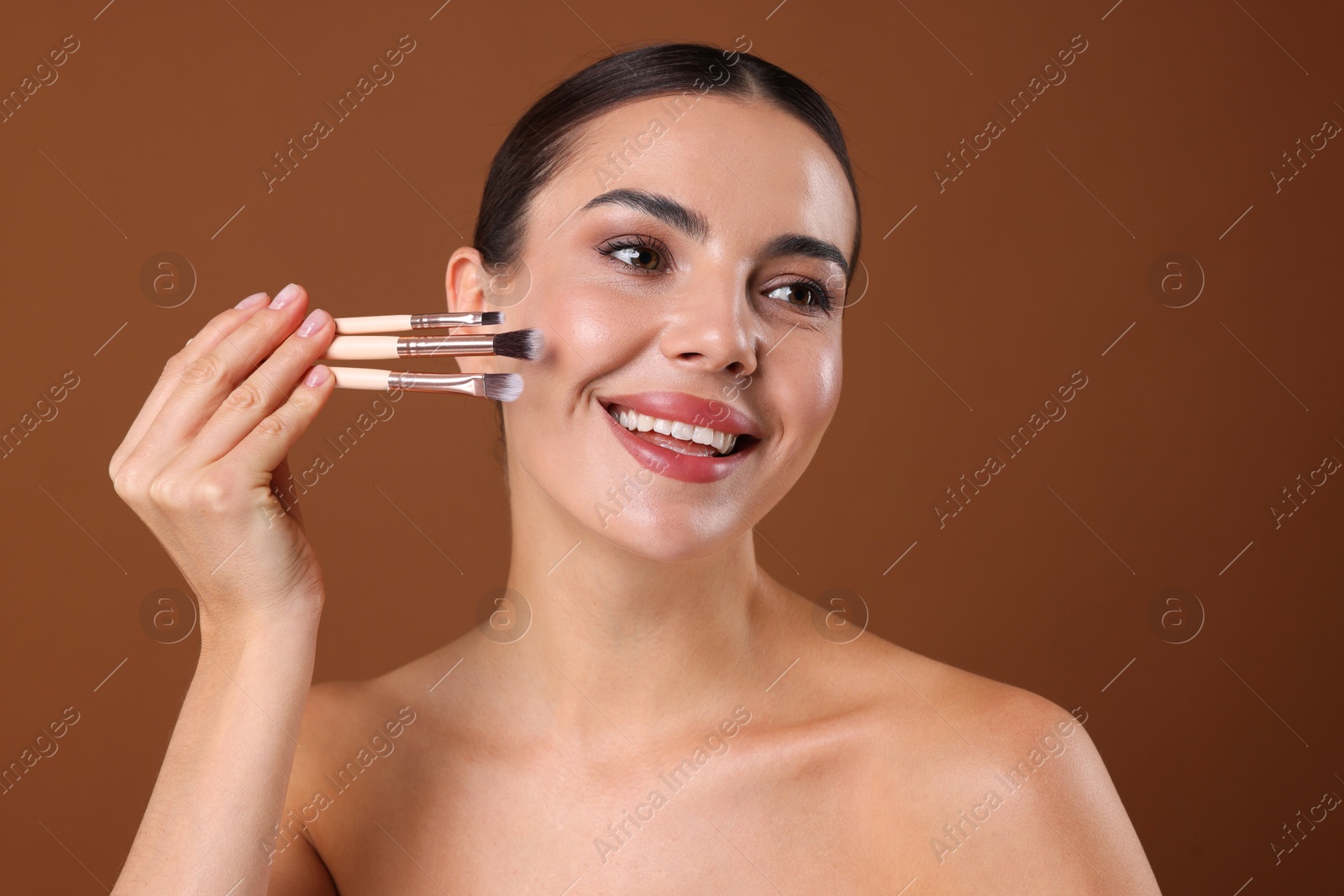 Photo of Beautiful woman with makeup brushes on brown background
