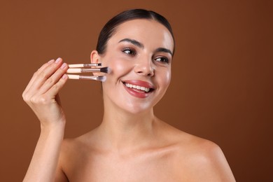 Photo of Beautiful woman with makeup brushes on brown background