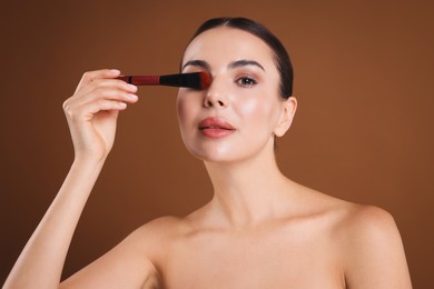Photo of Beautiful woman with makeup brush on brown background