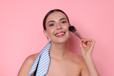 Photo of Beautiful woman applying makeup with brush on pink background