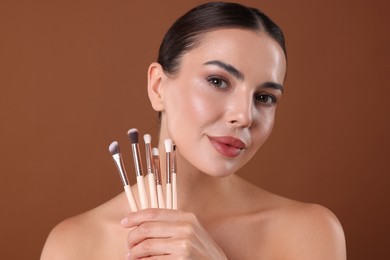 Photo of Beautiful woman with makeup brushes on brown background