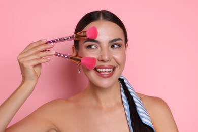 Photo of Beautiful woman with makeup brushes on pink background