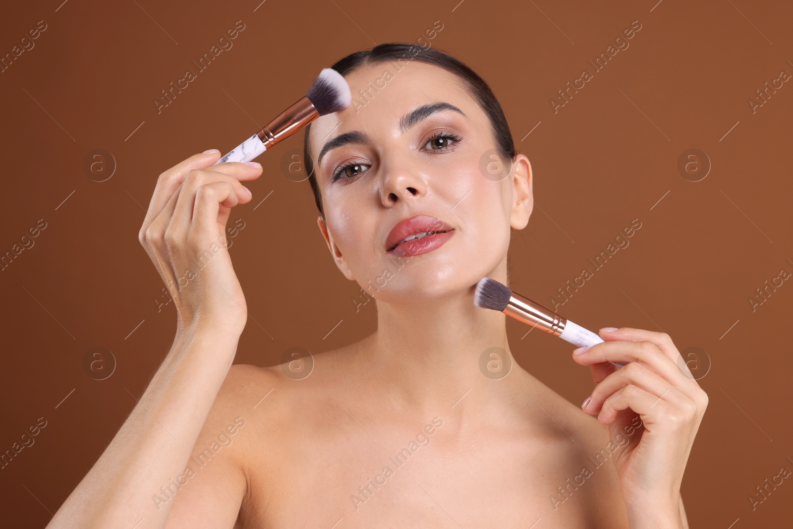 Photo of Beautiful woman with makeup brushes on brown background