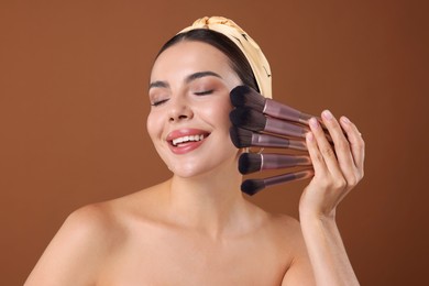 Photo of Beautiful woman with makeup brushes on brown background
