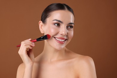 Photo of Beautiful woman applying makeup with brush on brown background