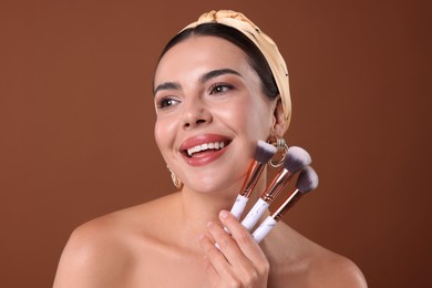 Photo of Beautiful woman with makeup brushes on brown background