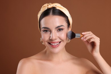 Photo of Beautiful woman applying makeup with brush on brown background