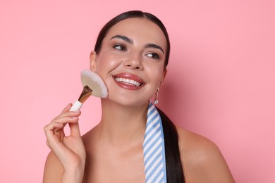 Photo of Beautiful woman applying makeup with brush on pink background