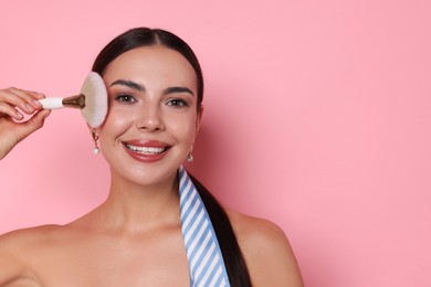 Photo of Beautiful woman applying makeup with brush on pink background, space for text