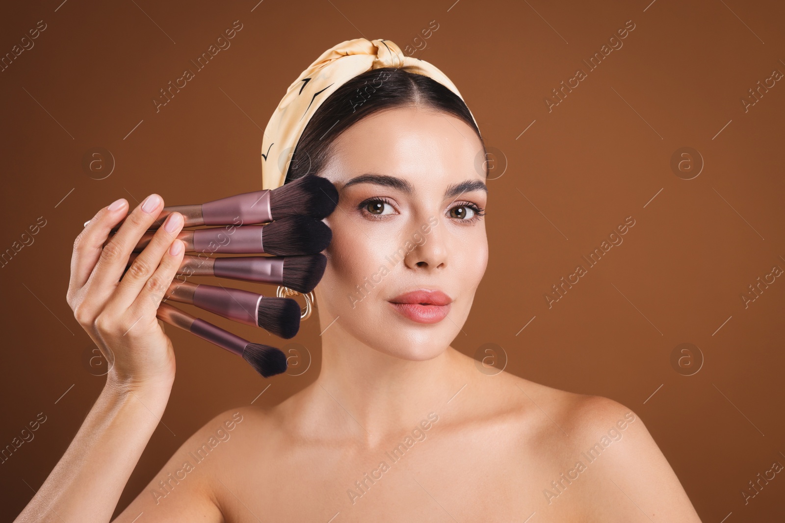 Beautiful woman with makeup brushes on brown background Photo of Beautiful woman with makeup brushes on brown background