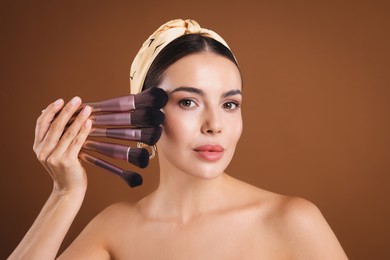 Photo of Beautiful woman with makeup brushes on brown background