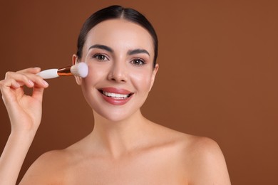 Photo of Beautiful woman applying makeup with brush on brown background, space for text