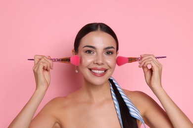 Photo of Beautiful woman with makeup brushes on pink background