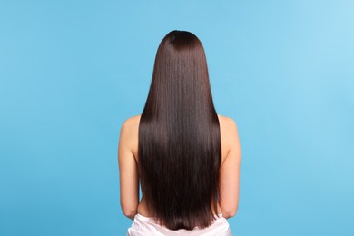 Photo of Woman with beautiful smooth hair after lamination procedure on light blue background, back view