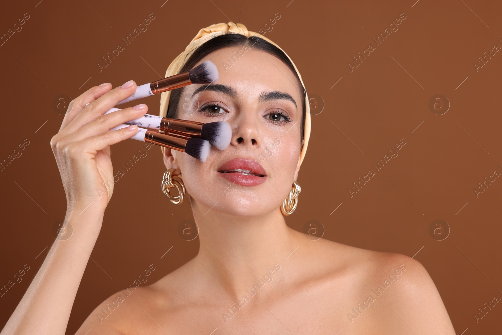 Beautiful woman with makeup brushes on brown background Photo of Beautiful woman with makeup brushes on brown background