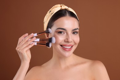 Photo of Beautiful woman with makeup brushes on brown background