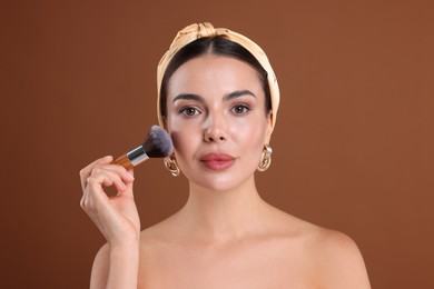 Photo of Beautiful woman applying makeup with brush on brown background