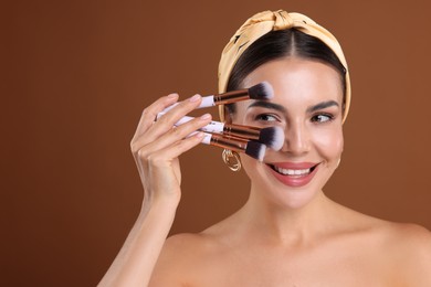 Photo of Beautiful woman with makeup brushes on brown background