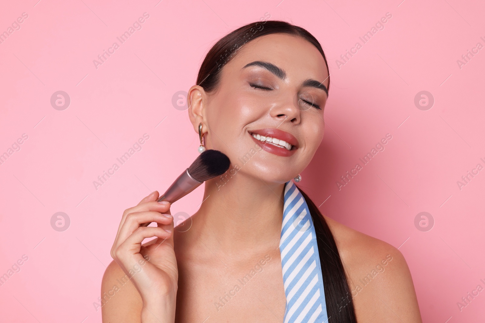 Beautiful woman applying makeup with brush on pink background Photo of Beautiful woman applying makeup with brush on pink background