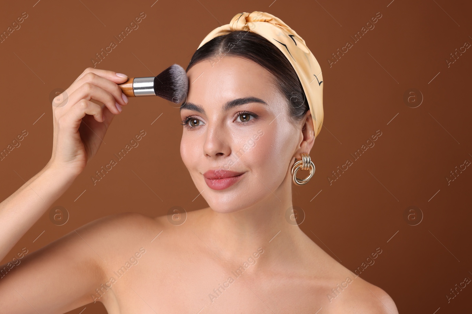Beautiful woman applying makeup with brush on brown background Photo of Beautiful woman applying makeup with brush on brown background